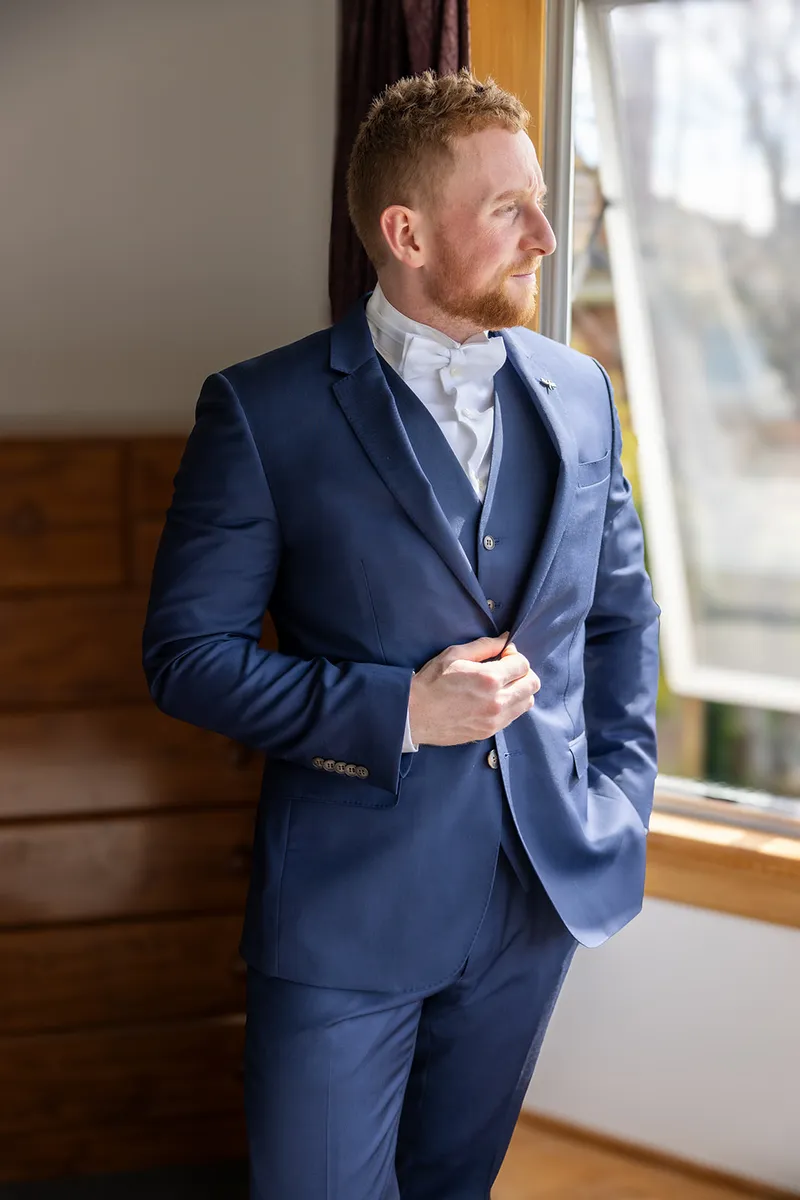 Groom looking out a window before his wedding ceremony