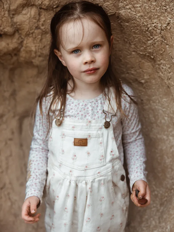 Young girl in floral overalls leaning against a clay wall, Eye Photography children's portrait portfolio