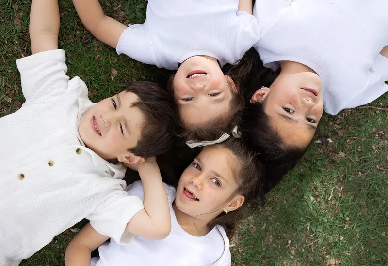 Four children laughing together on the grass during a family session