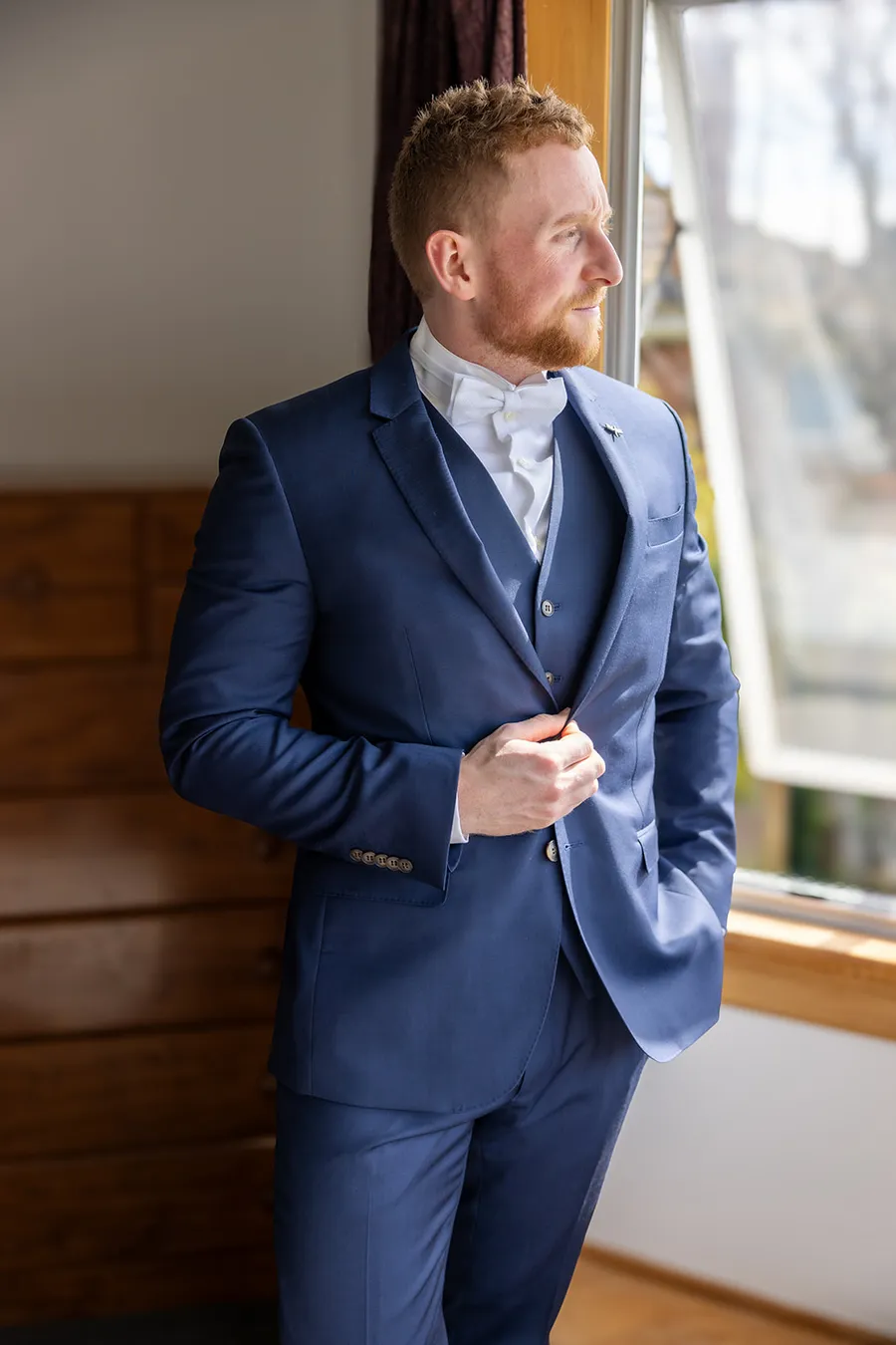 Groom getting ready by a window before his wedding